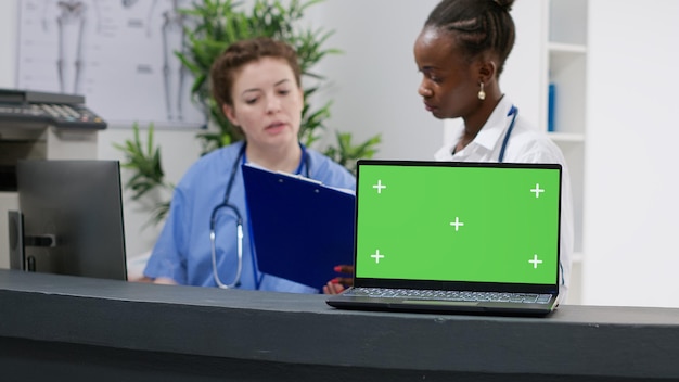 Computer portatile con display a schermo verde sul bancone della reception dell'ospedale utilizzato dall'équipe medica. Lavorare con il modello di copyspace vuoto, il mockup isolato e lo sfondo della chiave cromatica sul computer pc.