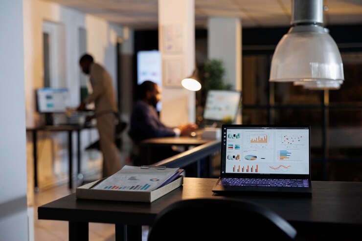 Foto computer portatile con grafici di dati finanziari in piedi sul tavolo della scrivania nell'ufficio di avvio, colleghi che lavorano a tarda notte alla strategia aziendale. dipendenti afroamericani che fanno brainstorming di idee imprenditoriali