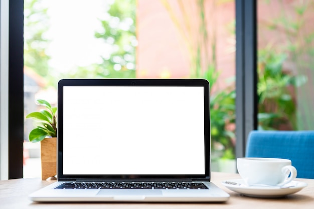 Computer portatile con lo schermo vuoto con la tazza di caffè sul tavolo della caffetteria. Schermo bianco