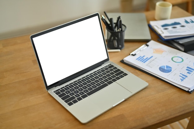Computer portatile con schermo bianco e documento grafico finanziario su tavolo di legno