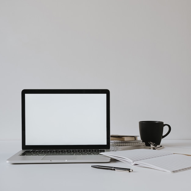 Computer portatile con schermo spazio copia vuoto sul tavolo con tazza di caffè, foglio di carta contro il muro bianco