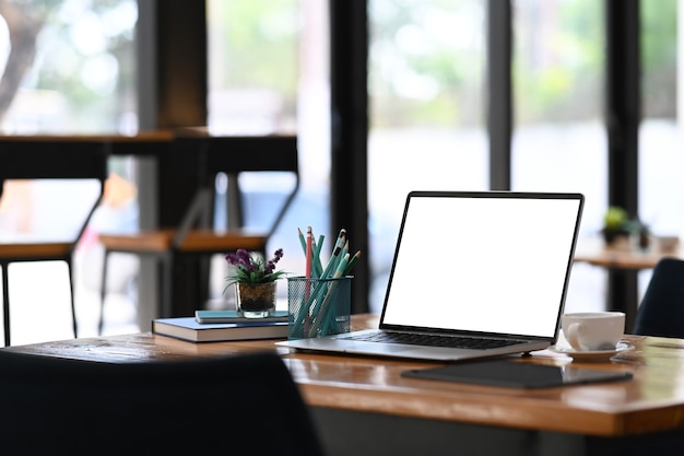 Computer portatile con schermo vuoto, forniture per ufficio annuncio tazza di caffè sulla scrivania in legno