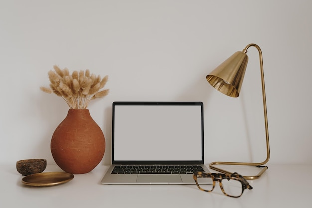 Computer portatile con schermo vuoto per la copia sul tavolo con cancelleria sul tavolo contro il muro bianco Area di lavoro minimalista per l'home office Modello mockup