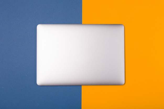 Computer portatile d'argento su contrasto fondo arancio e blu luminoso. Spazio libero. Copia spazio.