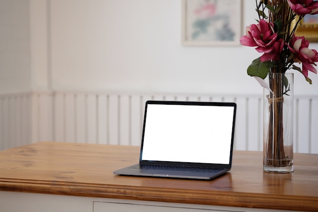 Computer portatile del modello e fiore rosa sulla scrivania di legno.