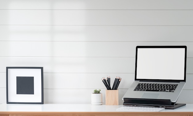 Computer portatile dello schermo in bianco del modello sul supporto e struttura di legno sulla tavola di legno con la parete di legno bianca.