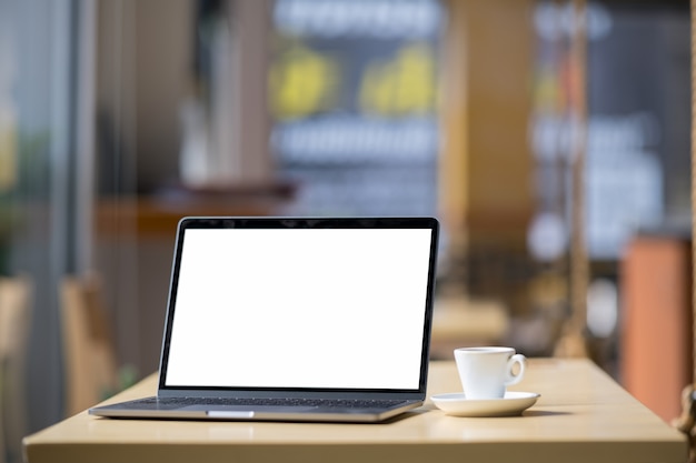 Computer portatile dello schermo in bianco del modello sulla tavola nel fondo del caffè.