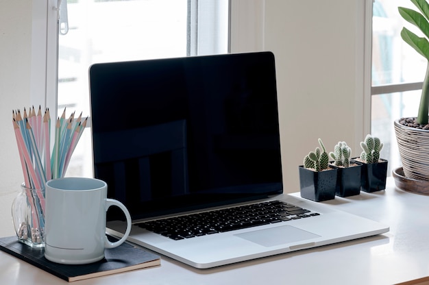 Computer portatile dello schermo in bianco nella stanza minima dell'ufficio con le decorazioni