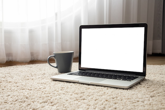 Computer portatile dello schermo in bianco, taccuino e tazza di caffè di mattina sul fondo di struttura del pavimento dello zerbino.