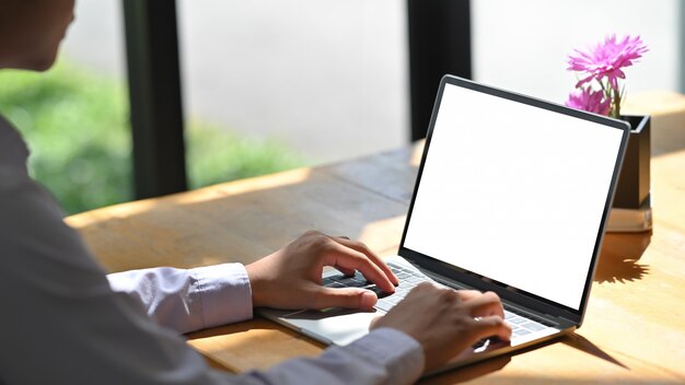 Computer portatile di battitura a macchina del modello dell'uomo del primo piano sulla tavola di legno.