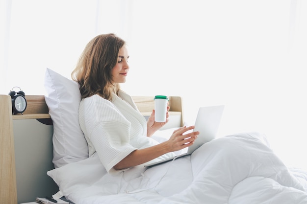 Computer portatile di lavoro digitale di lavoro della donna sul letto che lavora nella camera da letto a casa