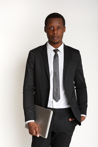 Computer portatile di trasporto dell'uomo d'affari serio isolato. Uomo afroamericano in piedi e tenendo il taccuino chiuso, sfondo bianco.