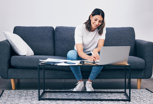 Computer portatile donna e appunti di scrittura sul divano del soggiorno durante il lavoro a distanza o lo studio sul tavolo a casa Libera professionista femminile che lavora con il sorriso per la strategia di pianificazione o notebook dal computer seduto sul divano