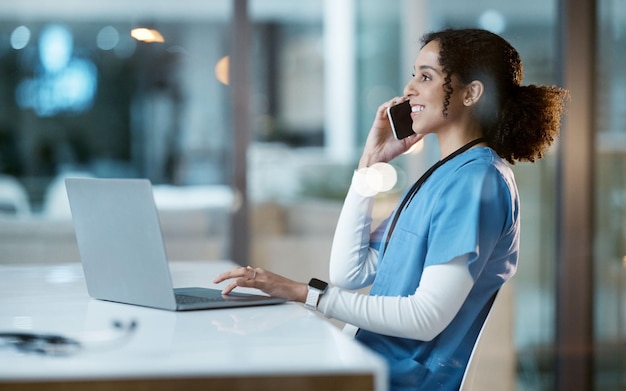 Computer portatile donna nera e infermiera durante una telefonata in ospedale conversazione e networking Smartphone notte e felice medico femminile che lavora fino a tardi telemedicina o consulenza per supporto in clinica