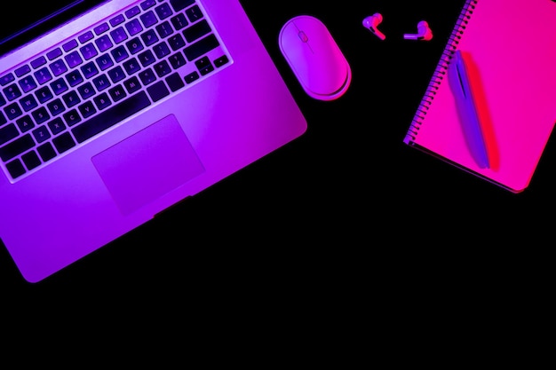Computer portatile e blocco note su sfondo nero con luce al neon piatta