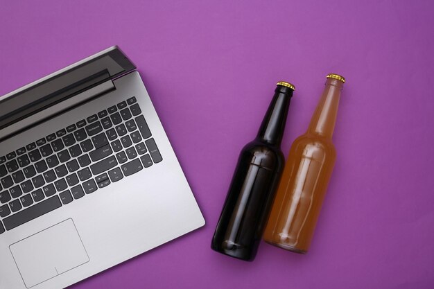 Computer portatile e bottiglie di birra su sfondo viola. Vista dall'alto