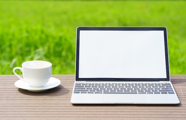 Computer portatile e tazza di cofree sul campo di erba verde dell'agente della tavola di legno in campagna