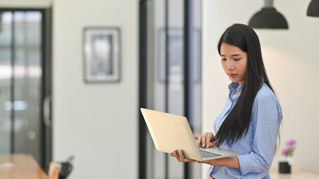 Computer portatile funzionante della giovane donna creativa nella stanza dell'ufficio.