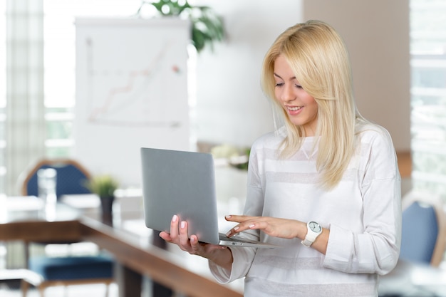 Computer portatile maturo sorridente della tenuta della donna