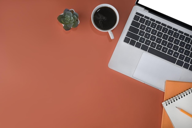 Computer portatile notebook e tazza di caffè su sfondo arancione Luogo di lavoro elegante Vista dall'alto