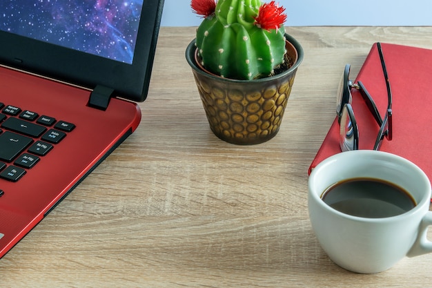 Computer portatile per lavorare, una tazza di caffè, cactus, occhiali e taccuino per prendere appunti.