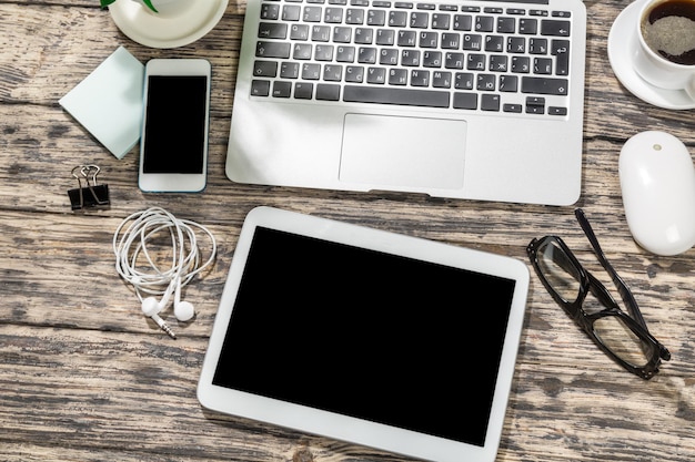 Computer portatile, smartphone, tablet e tazza di caffè con documenti finanziari sul tavolo di legno