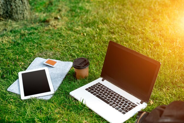 Computer portatile su erba verde con borsa per tazza di caffè e tablet nel parco all'aperto