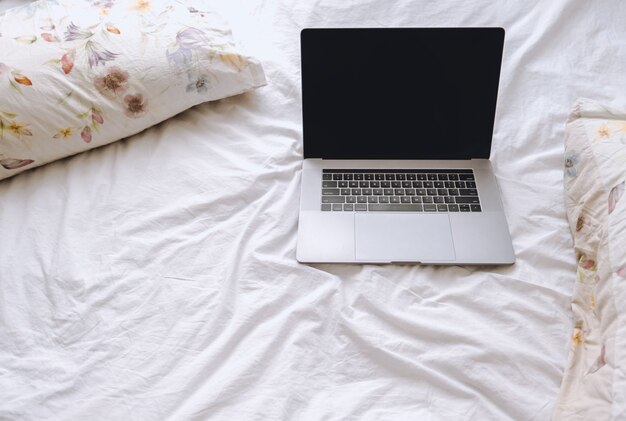 Computer portatile su un letto bianco con cuscini floreali. Lavoro a casa, concetto di libero professionista di lavoro a distanza