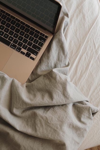 Computer portatile sul letto con biancheria da letto neutra Vista dall'alto spazio di lavoro bohémien di lusso estetico minimalista Flatlay