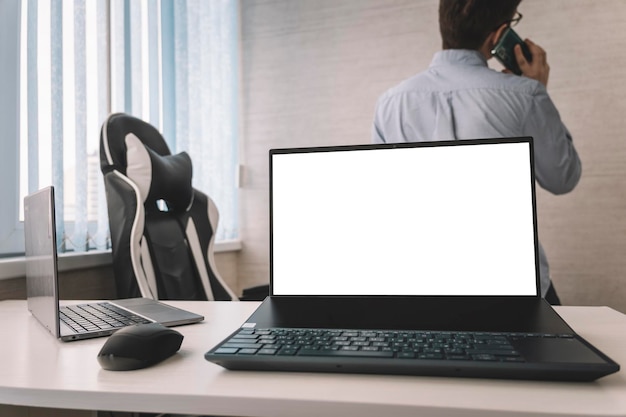 Computer portatile sul posto di lavoro in un ufficio bianco sullo sfondo di un dipendente che parla al telefono