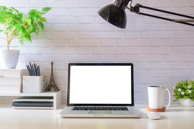 Computer portatile tazza di caffè e libro sul tavolo bianco contro il muro di mattoni Schermo vuoto per il tuo testo pubblicitario