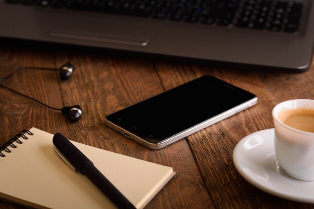 Computer portatile, telefono cellulare (smartphone) e blocco note con la penna sulla vecchia tavola di legno.