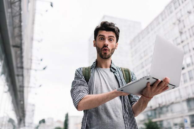 Computer portatile uscito della tenuta dell'uomo, comperante online, stante sulla via della città