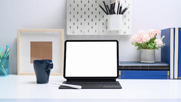 Computer tablet con schermo vuoto, libri e forniture per ufficio sul tavolo bianco