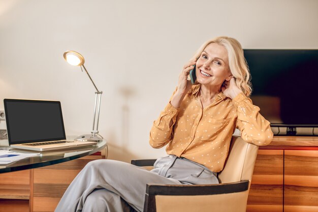 Comunicazione. Bella donna bionda seduta su una poltrona con un telefono in mano