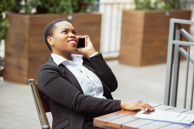 Comunicazione. Donna d'affari afro-americana in abbigliamento da ufficio sorridente, sembra sicura e felice, impegnata. Concetto di finanza, affari, uguaglianza e diritti umani. Bella giovane modella, di successo.