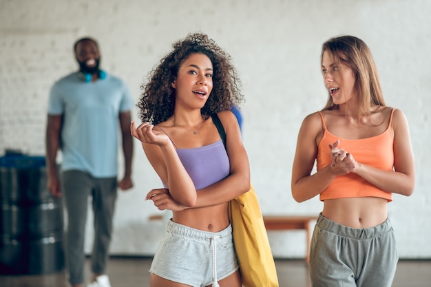 Comunicazione. Due giovani belle amiche snelle in abiti sportivi con borsa stanno parlando di ragazzi dietro