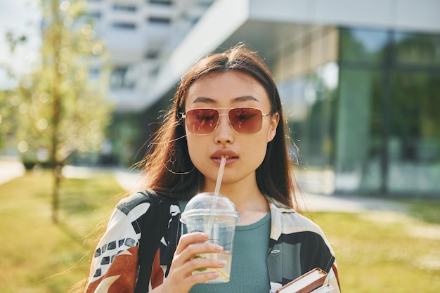 Con bevanda fresca La giovane donna asiatica è all'aperto durante il giorno