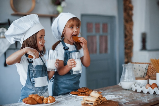 Con bicchieri di latte. Bambini di famiglia in uniforme bianca da chef che preparano il cibo in cucina.