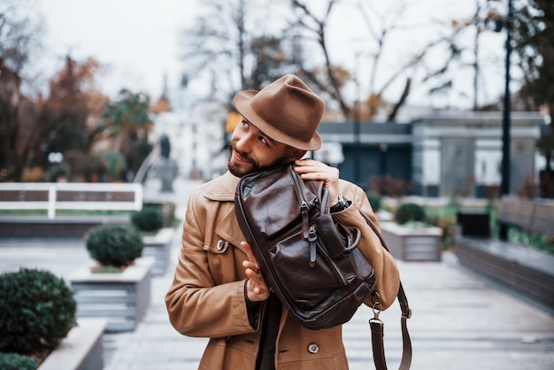 Con borsa Il giovane modello maschile in abiti alla moda è all'aperto in città durante il giorno