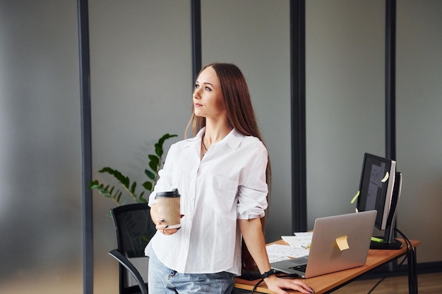 Con caffè Giovane donna adulta in abiti formali è al chiuso in ufficio