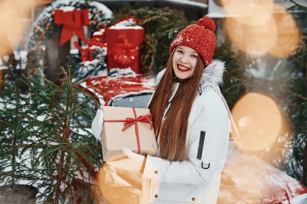 Con confezione regalo Felice giovane donna in piedi all'aperto e celebrare le vacanze di Natale