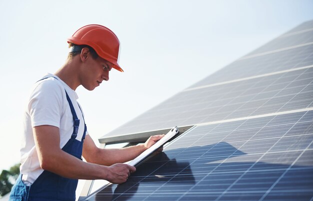 Con documenti. Lavoratore maschio in uniforme blu all'aperto con batterie solari al giorno pieno di sole.