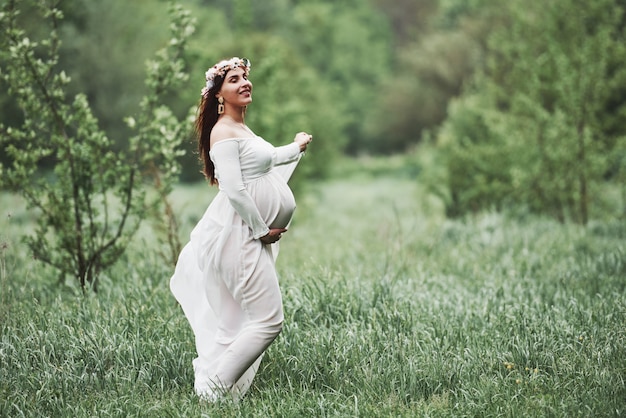 Con gli occhi chiusi. La bella donna incinta in vestito ha una passeggiata all'aperto. Bruna positiva