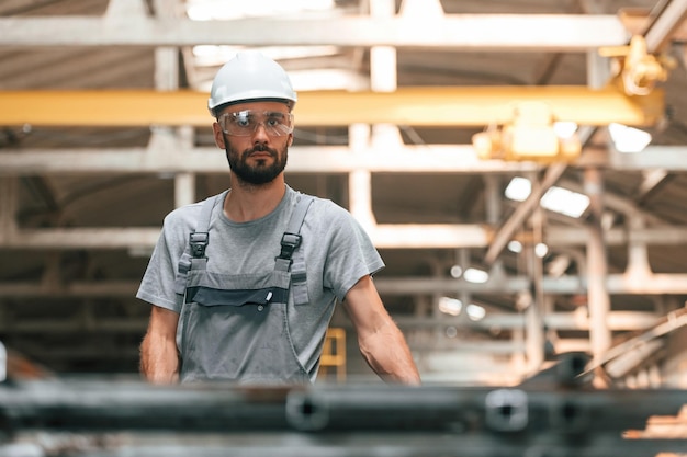 Con gli occhiali e il cappello bianco giovane operaio di fabbrica in uniforme grigio