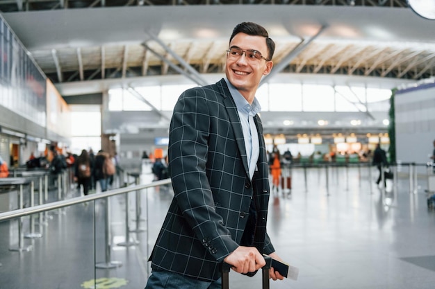 Con il bagaglio Il giovane uomo d'affari in abiti formali è in aeroporto durante il giorno