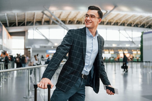 Con il bagaglio Il giovane uomo d'affari in abiti formali è in aeroporto durante il giorno