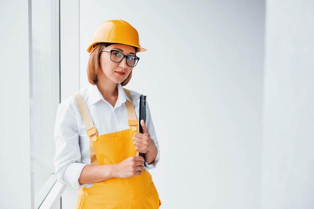 Con il blocco note in mano Operaia o ingegnere in uniforme gialla e elmetto in piedi all'interno