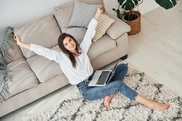 Con il computer portatile Bella giovane donna in jeans e camicia bianca è a casa