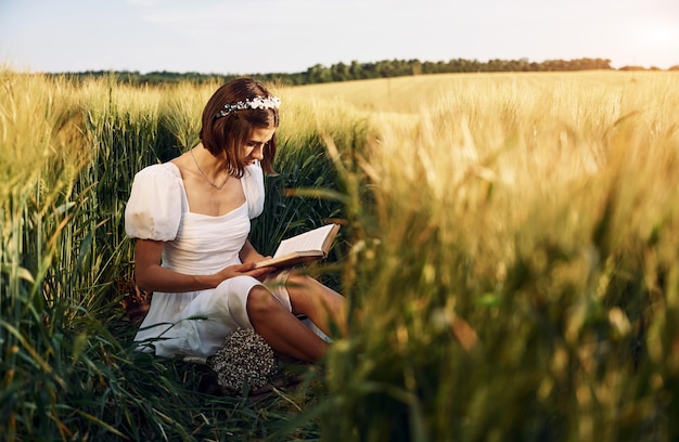 Con il libro Bella giovane sposa in abito bianco è sul campo agricolo in giornata di sole